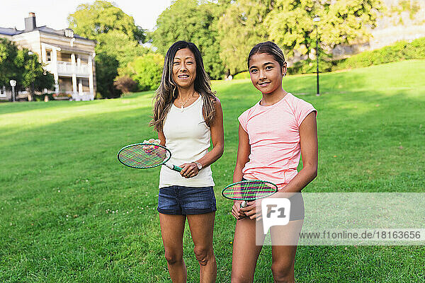 Mother and daughter with badminton racket standing on grass in lawn