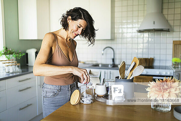 Happy woman filling glass jar at kitchen counter