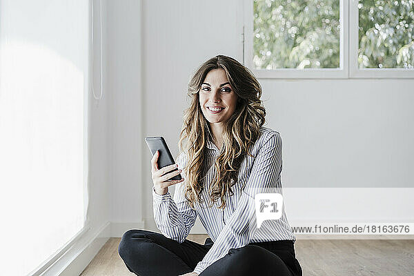 Smiling businesswoman in office using mobile phone by window