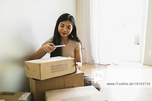 Woman taking picture of delivery package box through smart phone at home