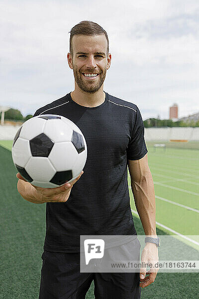 Smiling sportsman holding soccer ball on sports field