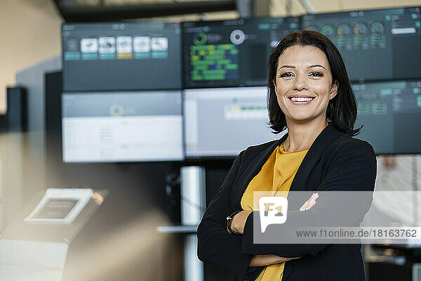 Smiling businesswoman with arms crossed in front of computer monitors
