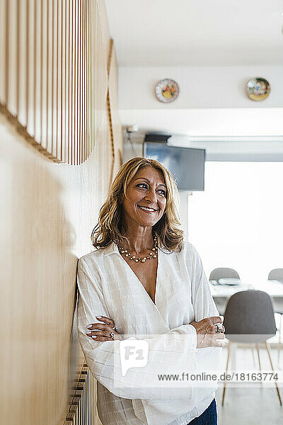 Happy businesswoman with arms crossed leaning on wall at restaurant