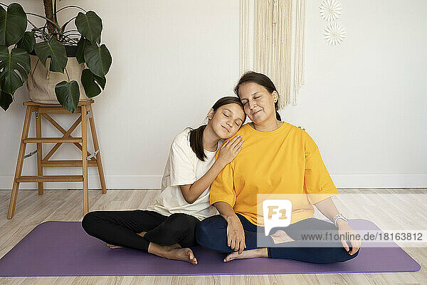 Smiling girl and woman sitting with eyes closed on exercise mat at home