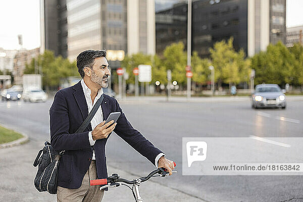 Smiling commuter with smart phone and bicycle at roadside