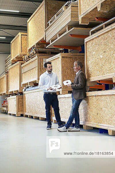 Senior businessman with colleague standing by storage compartment at warehouse