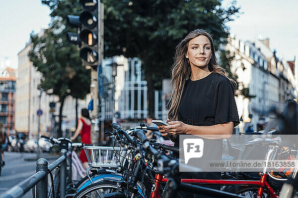 Young woman with smart phone standing at bicycle parking station