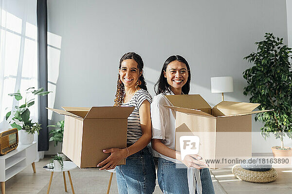 Lächelnde Freunde mit Pappkartons  die in ein neues Haus einziehen