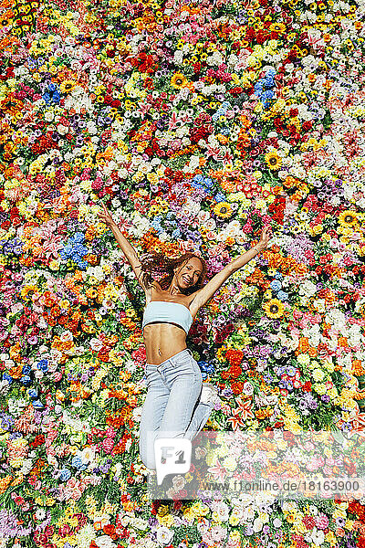 Glückliche junge Frau springt vor einer bunten Blumenwand