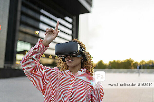 Junge Frau trägt VR-Brille und hebt die Hand auf dem Fußweg