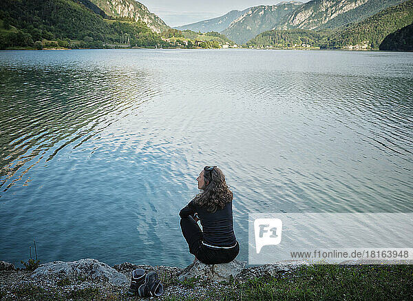 Mature woman sitting on rock at lakeshore