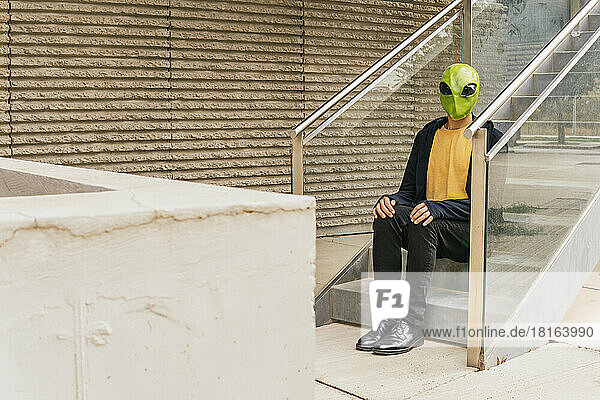 Mann mit Alien-Maske sitzt auf der Treppe
