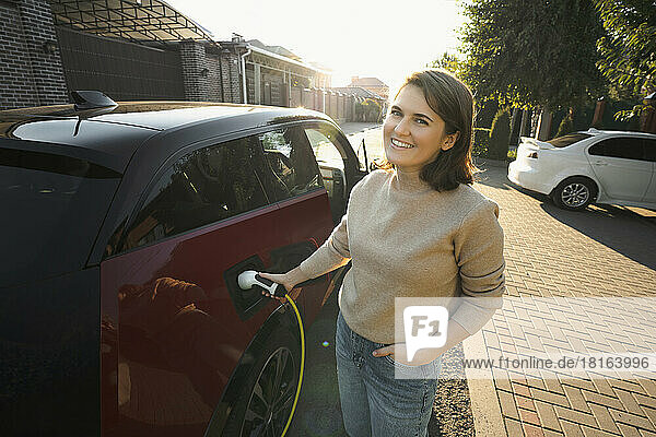 Happy woman charging electric car at roadside