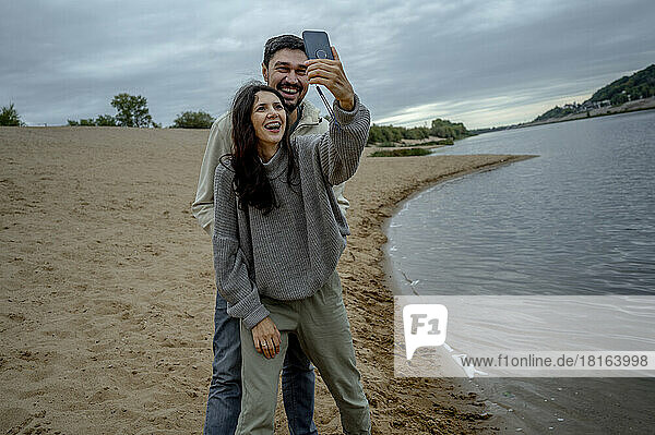 Glückliches Paar  das Spaß daran hat  ein Selfie mit dem Smartphone am Fluss zu machen