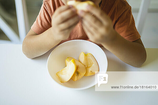 Slices of apple in bowl on table by boy at home