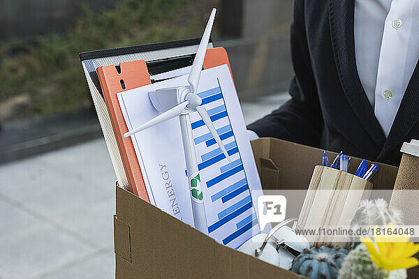 Businessman holding box with wind turbine model and documents