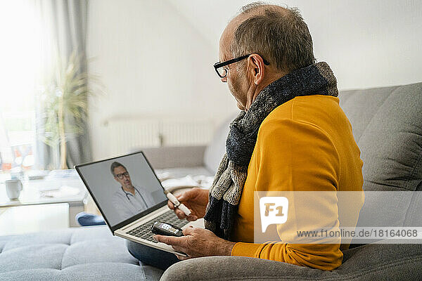 Man doing online consultation with doctor through laptop on sofa at home
