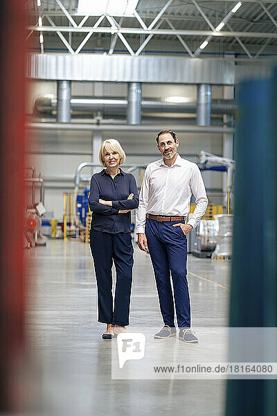Smiling businesswoman with arms crossed standing by colleague in industry