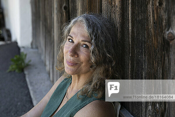 Smiling gray haired woman leaning on wooden door