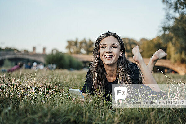 Happy woman with smart phone lying on grass at park