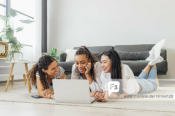 Lächelnde Mitbewohner schauen sich zu Hause im Wohnzimmer einen Film auf dem Laptop an