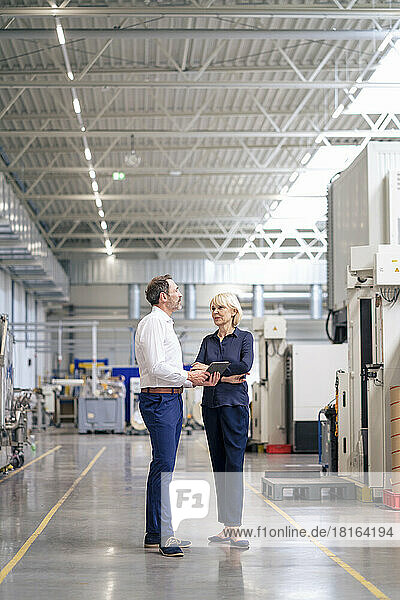 Businessman holding tablet PC discussing with colleague in factory
