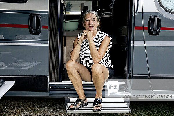Smiling senior woman sitting at doorway of camper van