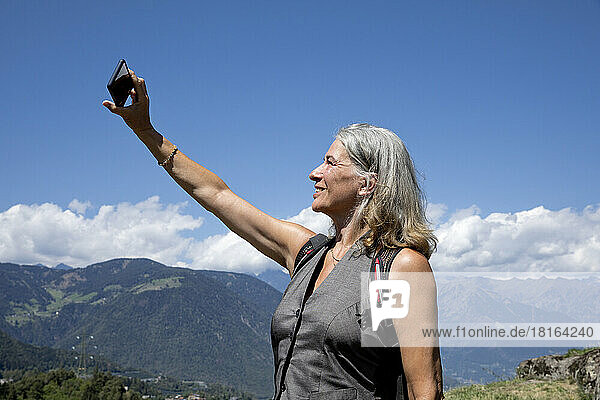 Smiling senior woman taking selfie through smart phone on sunny day