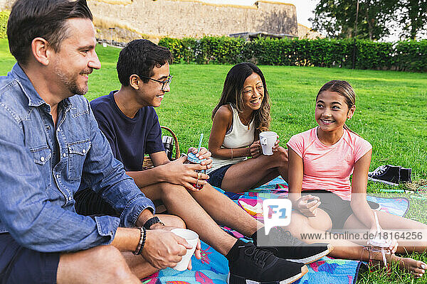 Gemischtrassige Familie genießt Getränke im Rasen beim Picknick