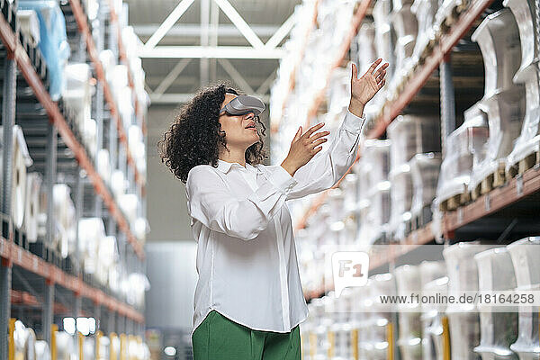 Businesswoman with futuristic glasses gesturing by rack in warehouse