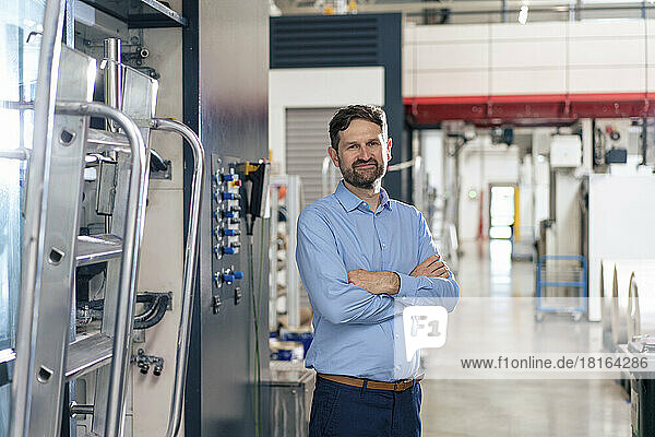 Smiling businessman standing by machine in factory