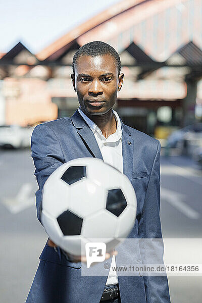 Businessman with soccer ball standing at parking lot on sunny day