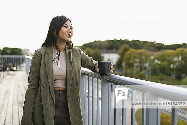 Thoughtful woman with coffee cup standing on terrace
