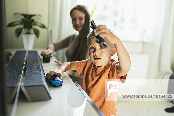 Boy playing with toy cars by mother in living room at home