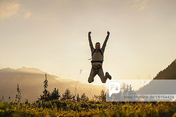 Glücklicher Mann springt bei Sonnenuntergang auf den Gipfel des Berges