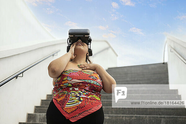 Smiling woman wearing virtual reality simulator in front of staircase