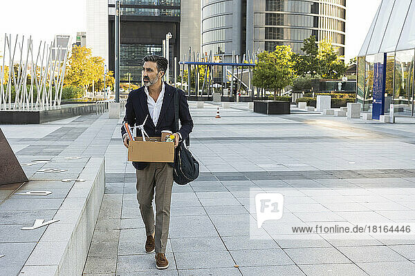 Geschäftsmann hält einen Karton in der Hand und läuft vor dem Bürogebäude