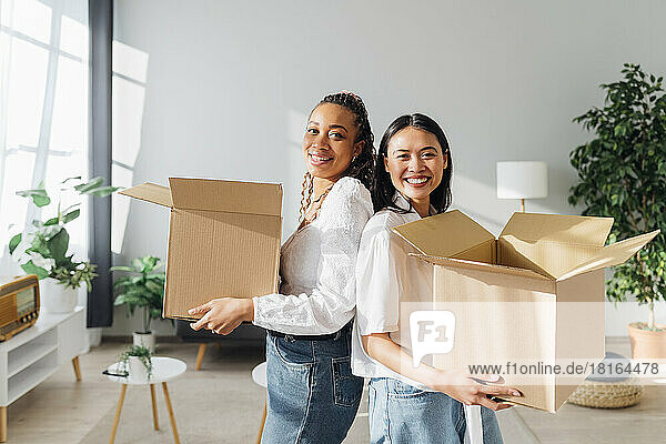 Happy friends with cardboard boxes moving in new house