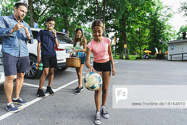 Girl playing with ball by family enjoying ice cream at parking lot