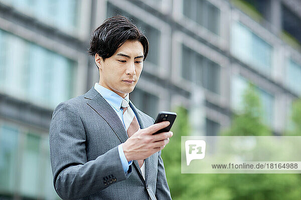Japanischer Geschäftsmann mit Blick auf ein Smartphone