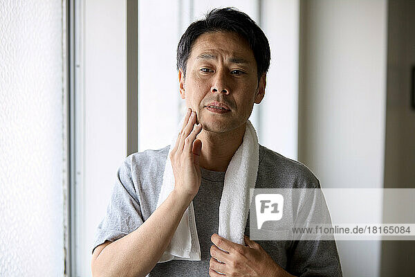 Japanese man touching his cheek with his hand