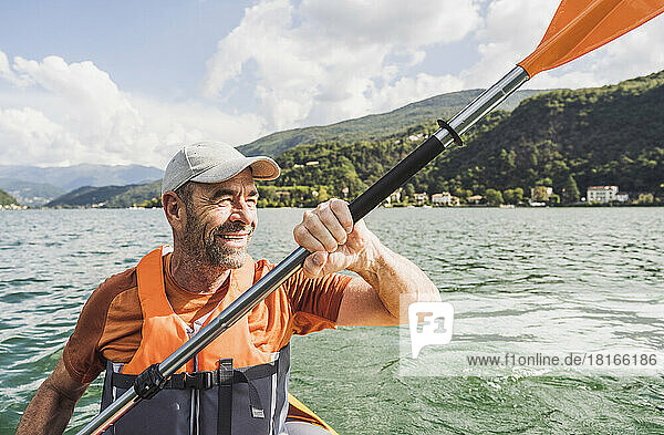 Lächelnder Mann  der an einem sonnigen Tag ein Kajakboot rudert