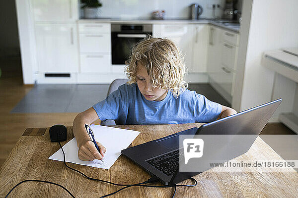 Boy doing homework with laptop on table at home