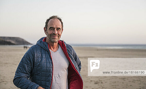 Smiling man wearing jacket in front of sky at beach