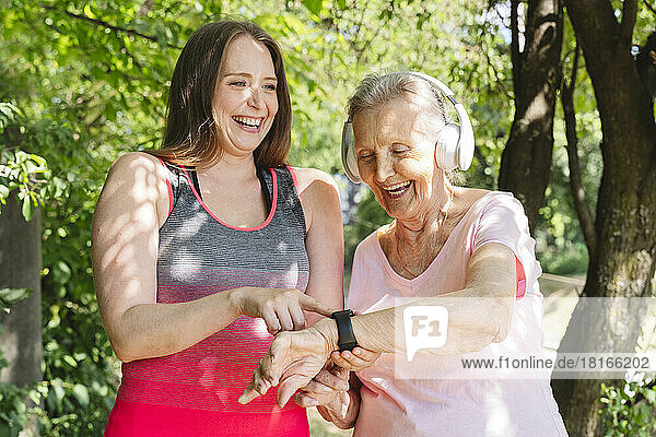Happy fitness instructor with senior woman wearing smart watch at park
