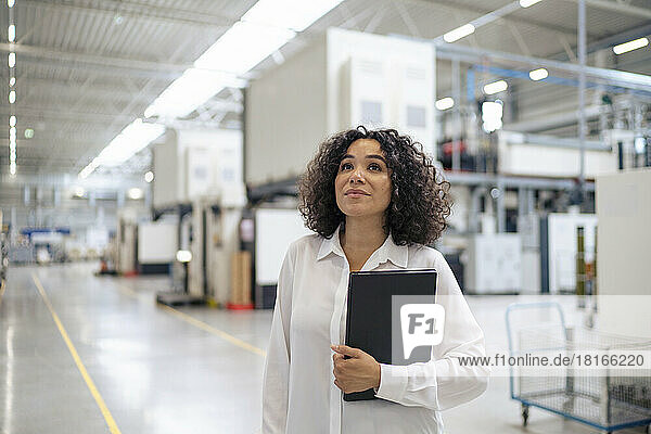 Thoughtful businesswoman holding laptop in factory