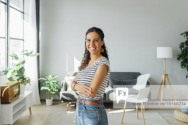 Happy woman with arms crossed standing in living room