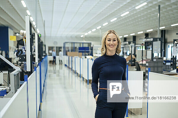 Smiling blond businesswoman with hands in pockets at factory