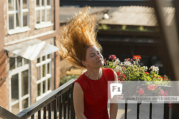 Smiling woman with eyes closed tossing hair on balcony