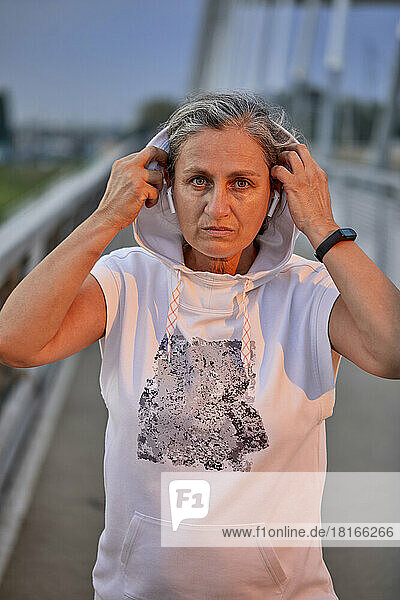 Confident woman with wireless in-ear headphones wearing hooded shirt